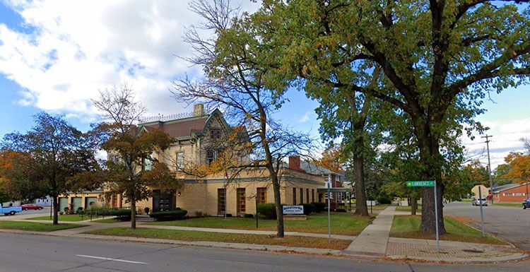 A large house is sitting on the corner of a street surrounded by trees.