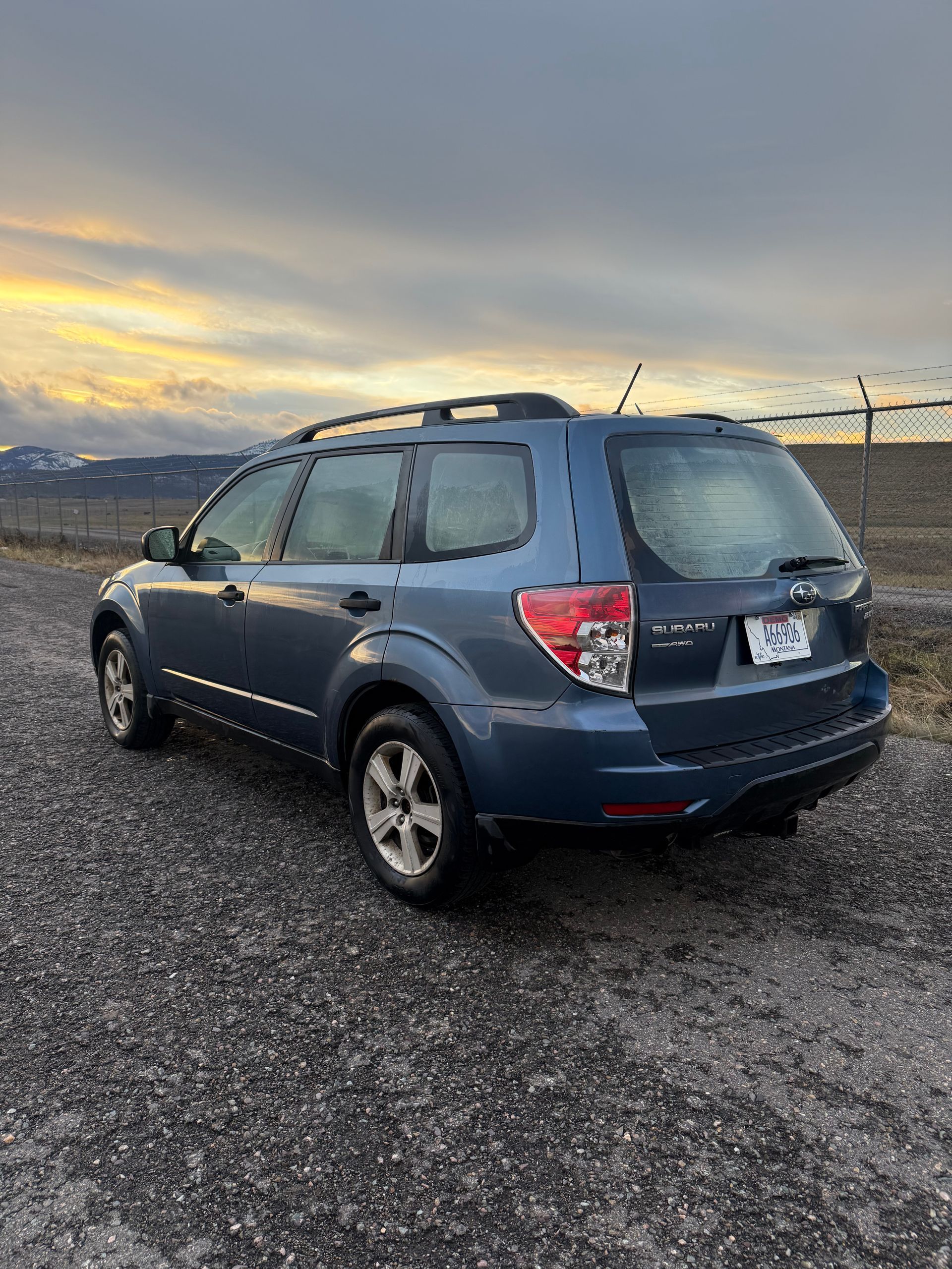 Blue Subaru Forester SUV parked on a gravel road, overcast sky.