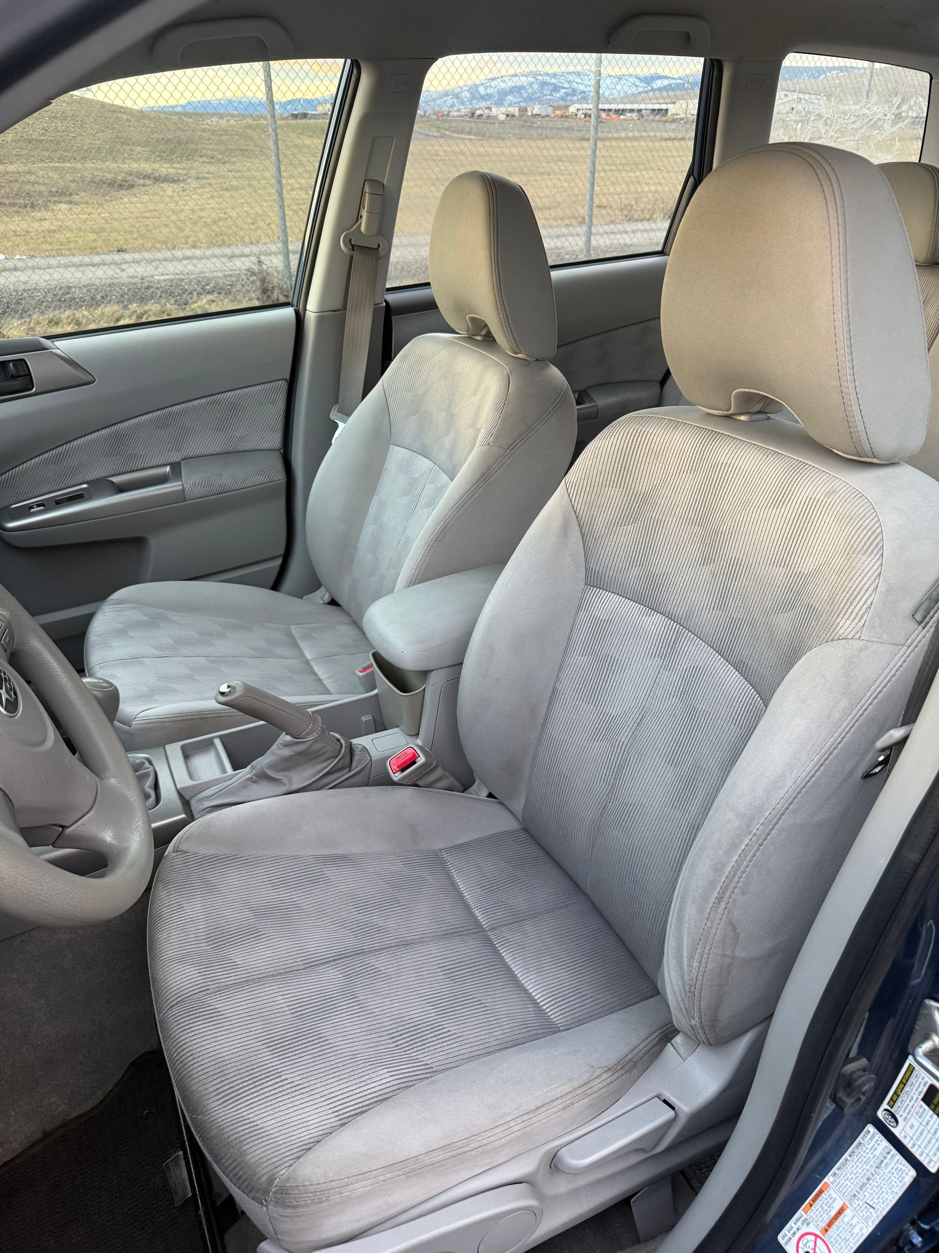 Interior of a car with light gray fabric seats. Front seats and steering wheel visible.