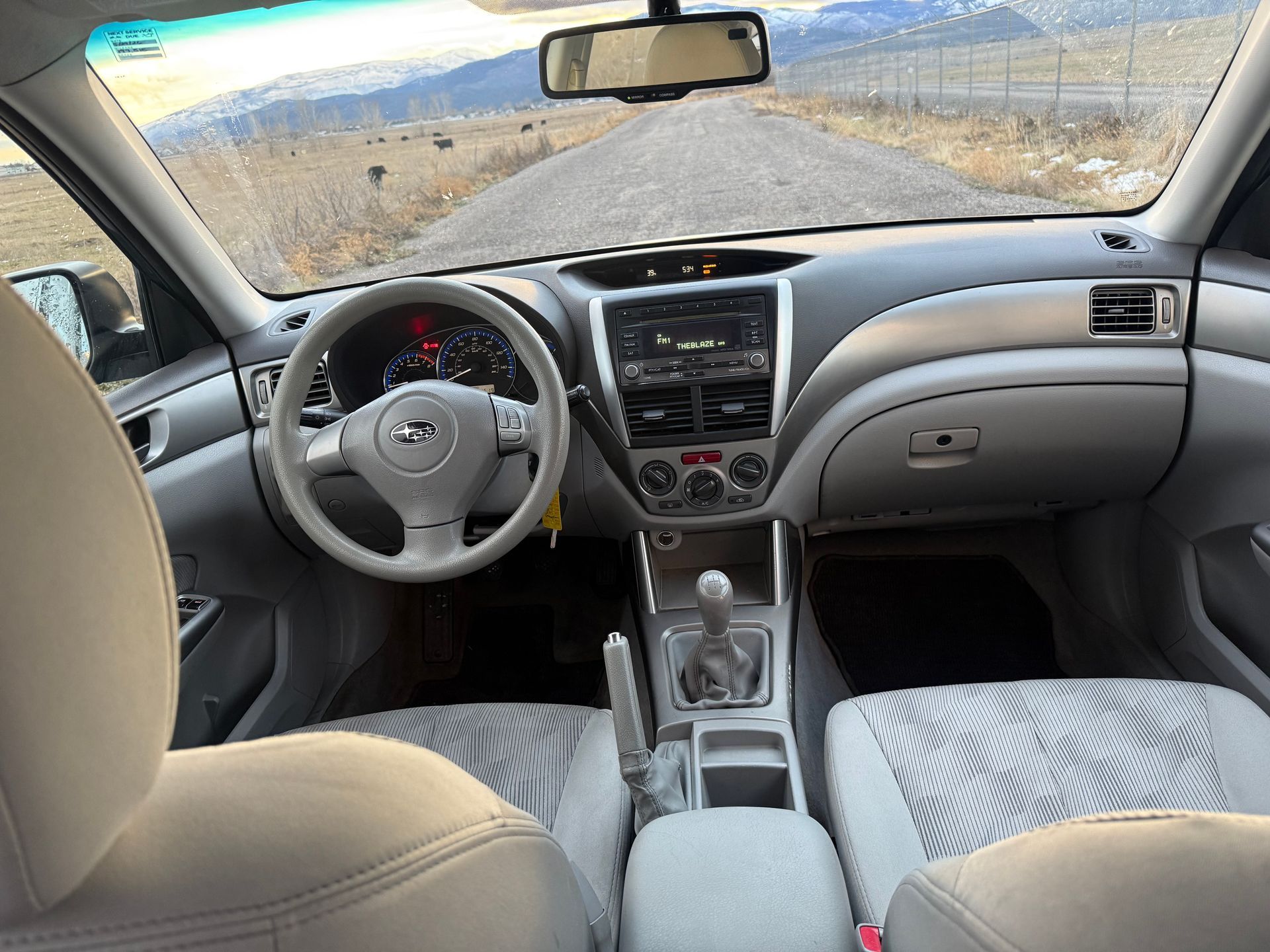 Interior view of a Subaru Forester's dashboard and front seats, overlooking a road with mountains in the background.