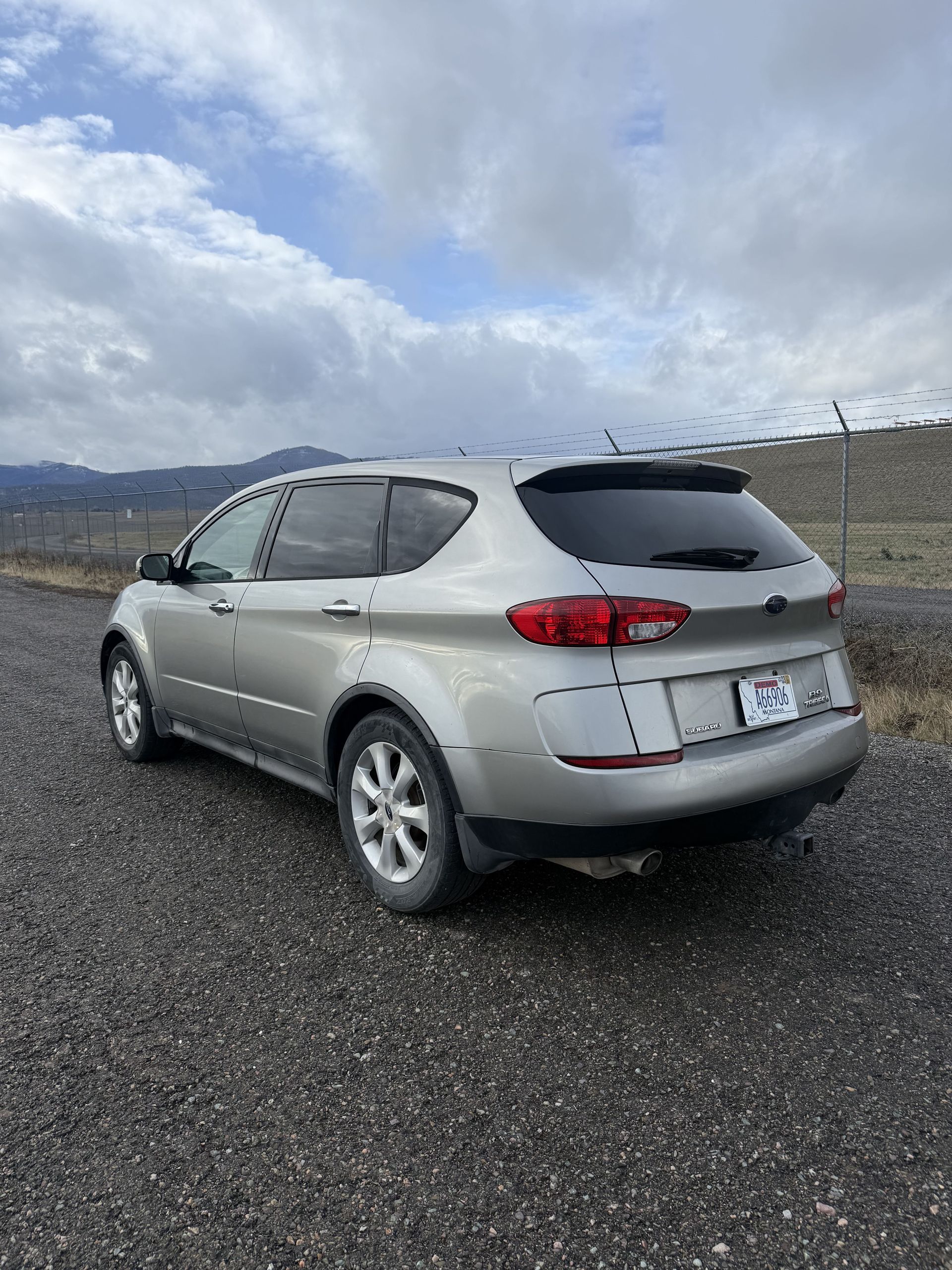 Silver Subaru Tribeca parked on a gravel road, overcast sky in the background.