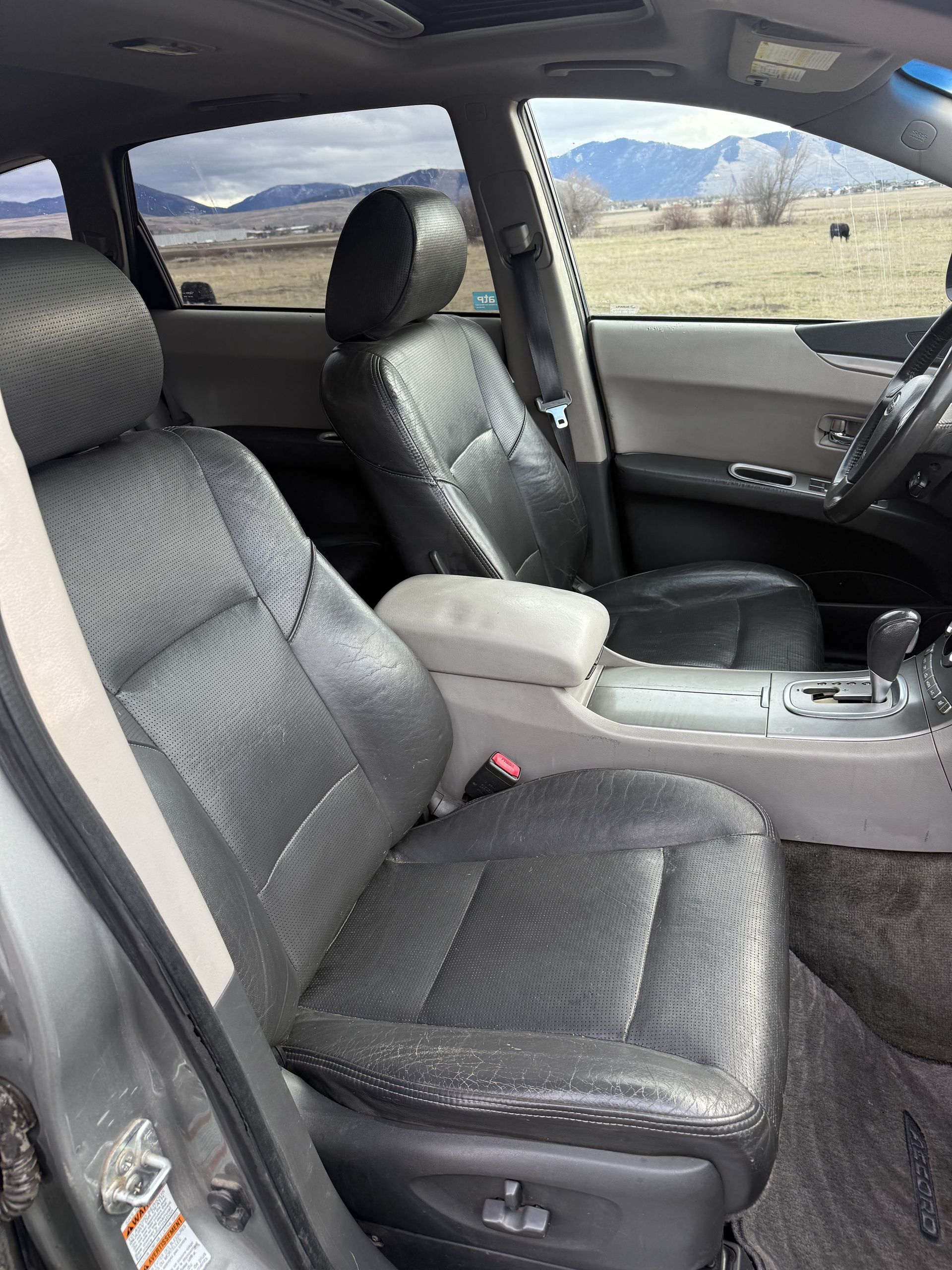 Interior of a gray Subaru Outback.  Black leather seats show wear.  A mountain range is visible through the window.
