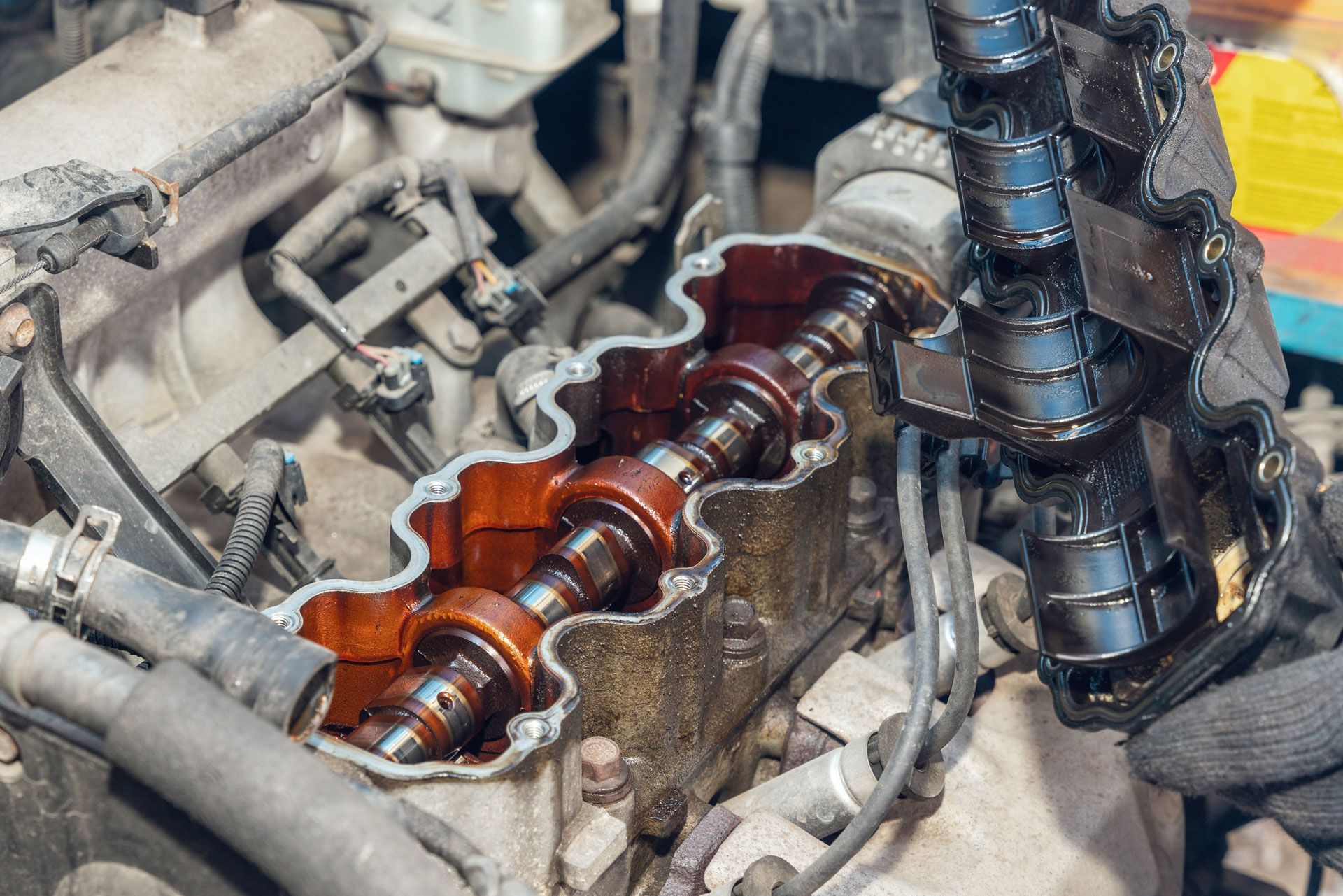 Open car engine with exposed camshafts and valve cover, covered in oil.