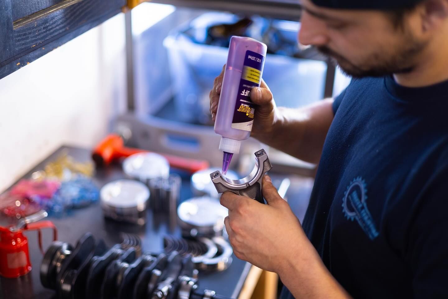 A man is holding a bottle of purple glue and applying it to a piece of metal.