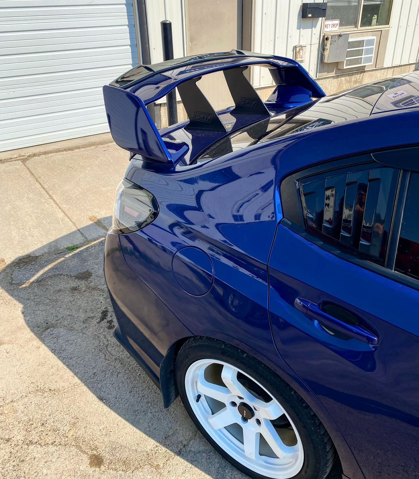 A blue car with a spoiler on the back is parked in front of a garage door.