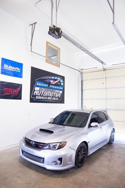 A silver subaru is parked in a garage under a garage door.