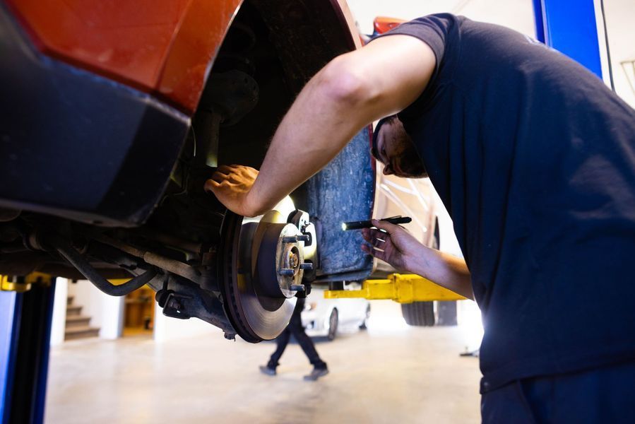 A man is working on a car on a lift in a garage.