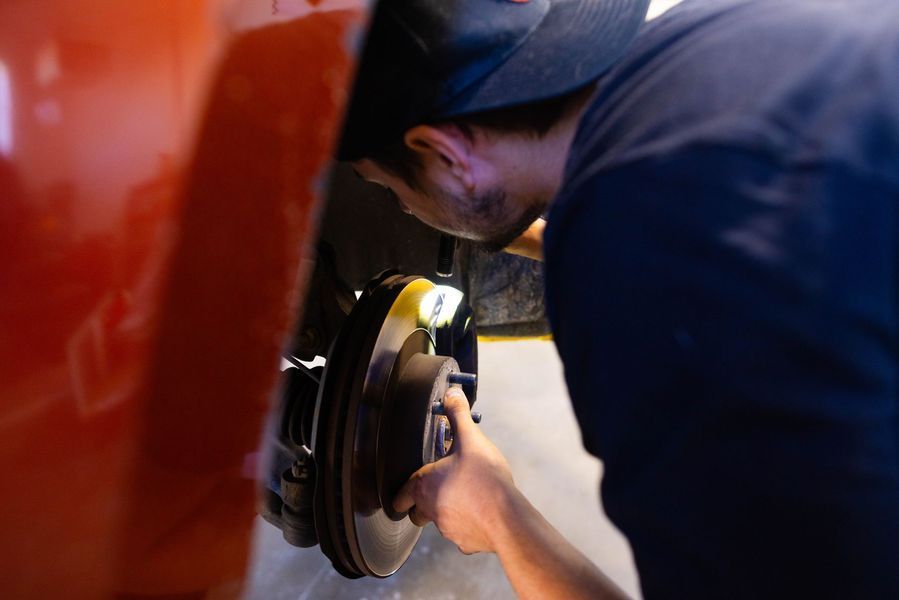 A man is working on a brake disc on a red car.