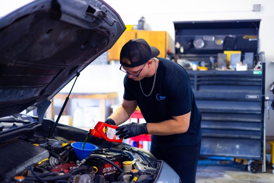 A man is pouring oil into a car engine in a garage.
