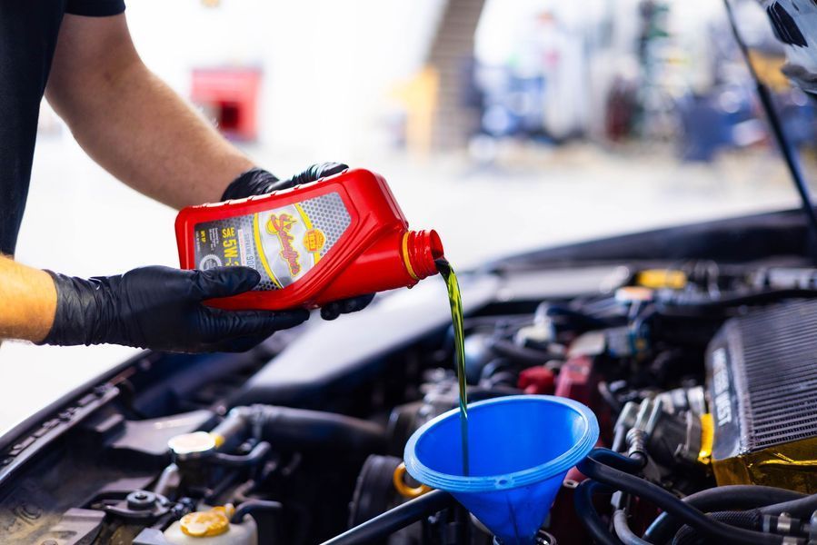 A man is pouring oil into a car through a funnel.