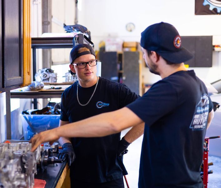 Two men in black shirts are talking in a garage