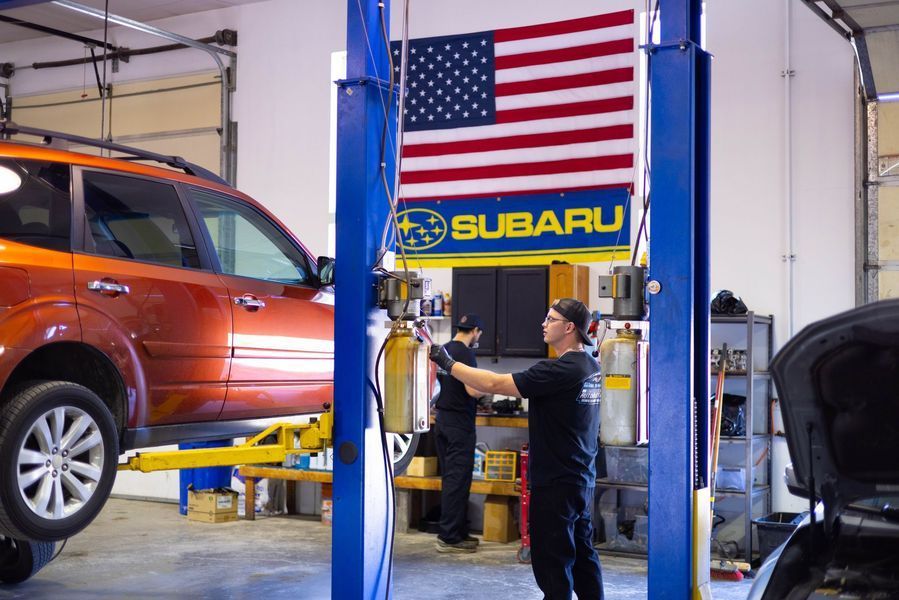 A man is working on a subaru car in a garage.