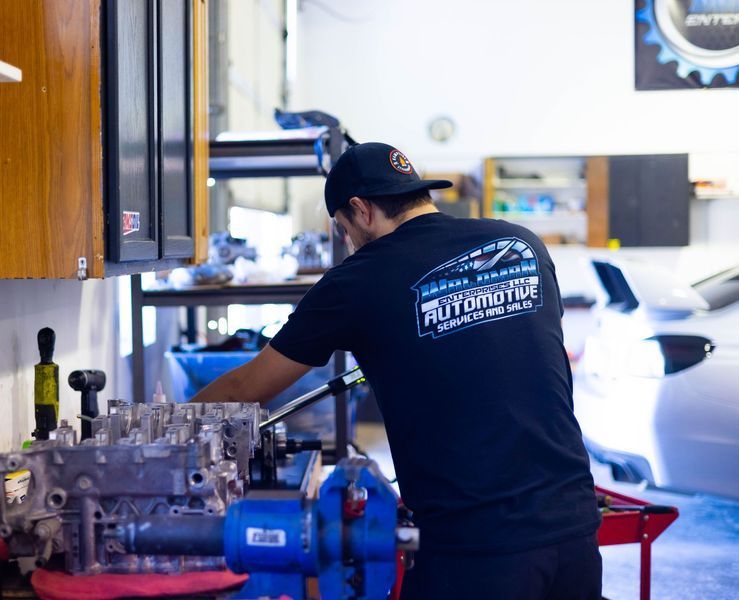 A man wearing a black shirt that says automotive is working on a car engine