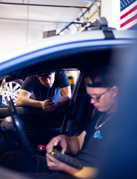 Two men are sitting in a car looking at their phones