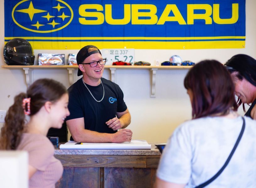 A man is talking to a group of people in front of a subaru banner.