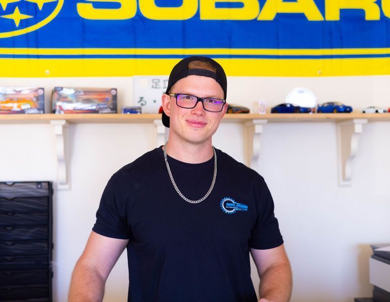 A man wearing glasses and a hat is standing in front of a subaru sign