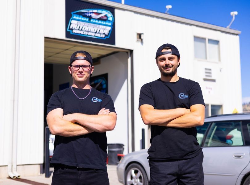 Two men are standing in front of a building with their arms crossed.