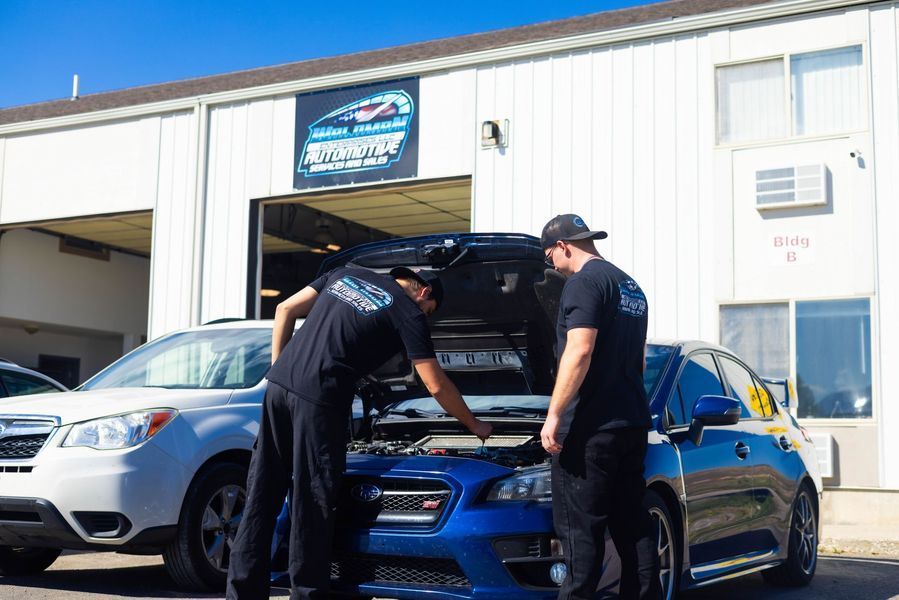 Two men are working on a car in front of a garage.