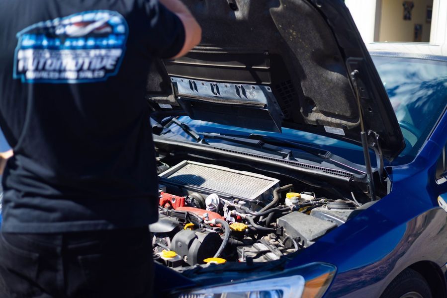 A man is looking under the hood of a blue car.