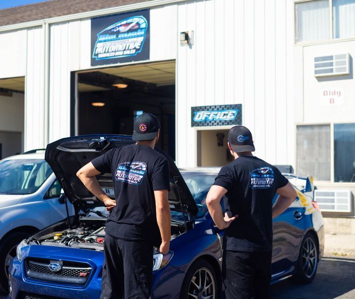 Two men standing next to a blue car with the hood open
