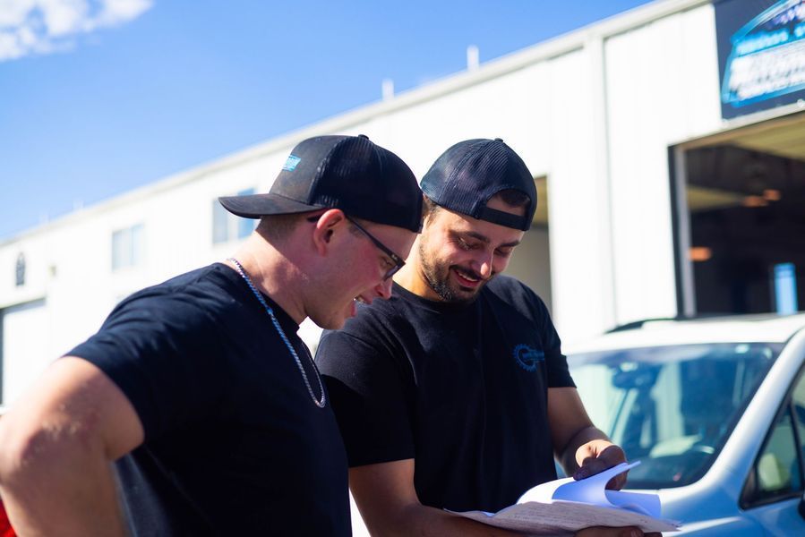 Two men are looking at a piece of paper in front of a car.