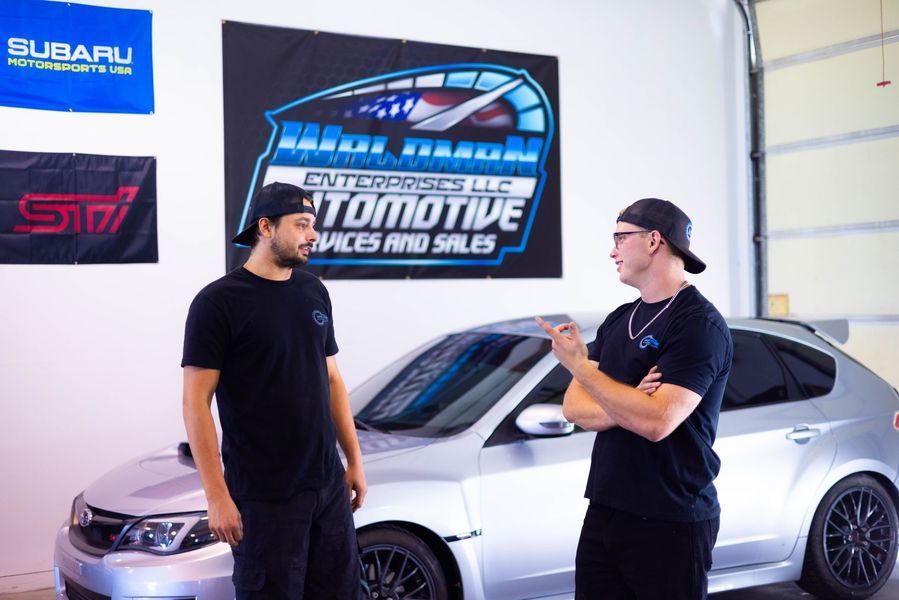 Two men are standing in front of a subaru car in a garage.