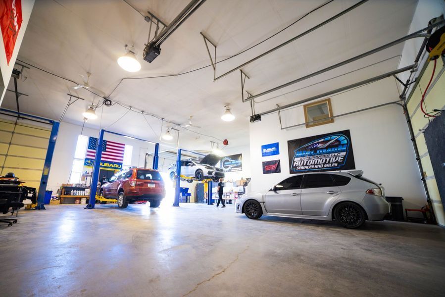 A car is parked in a garage with other cars on lifts.