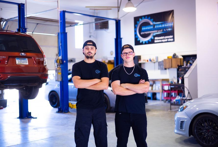 Two men are standing in a garage with their arms crossed.