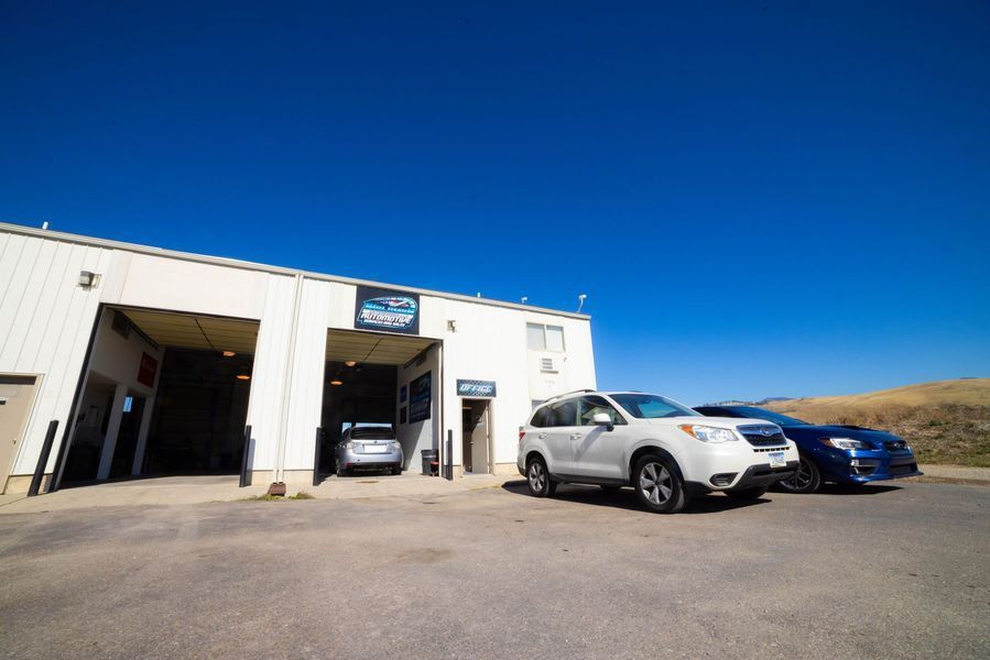 Three cars are parked in front of a car dealership.