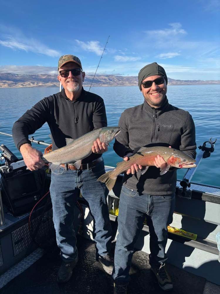 Two men are holding fish on a boat in the water.