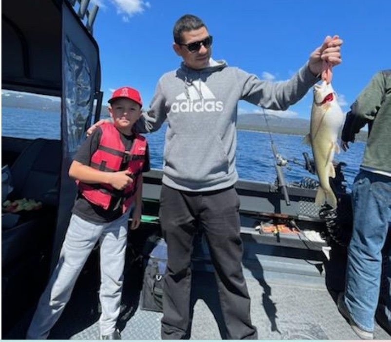 A man wearing an adidas sweatshirt is holding a fish
