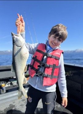 A young boy in a life jacket is holding a large fish.
