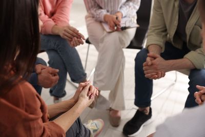 A group of people sitting in a circle during a support group meeting, with their hands clasped in their laps.