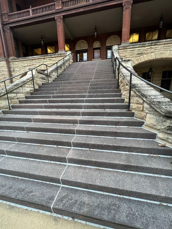 A construction worker in a red shirt and blue overalls places a brick on a partially built brick wall.