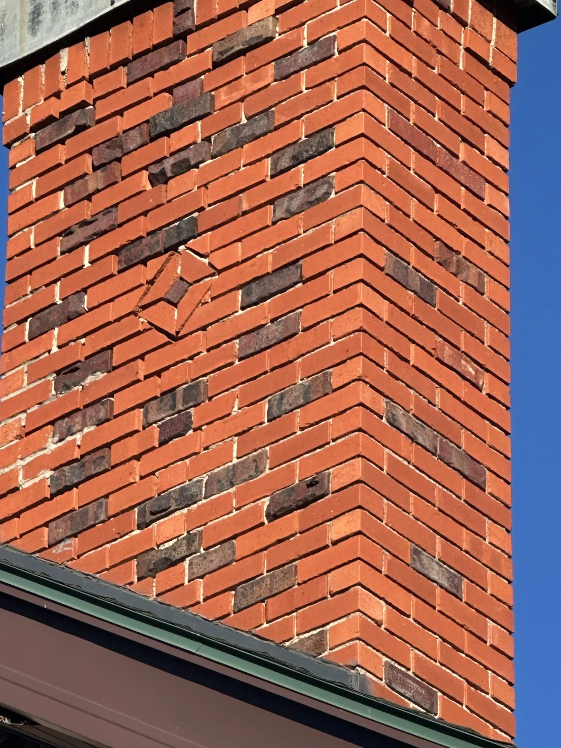 Brick chimney with patterned red and dark bricks against a blue sky.