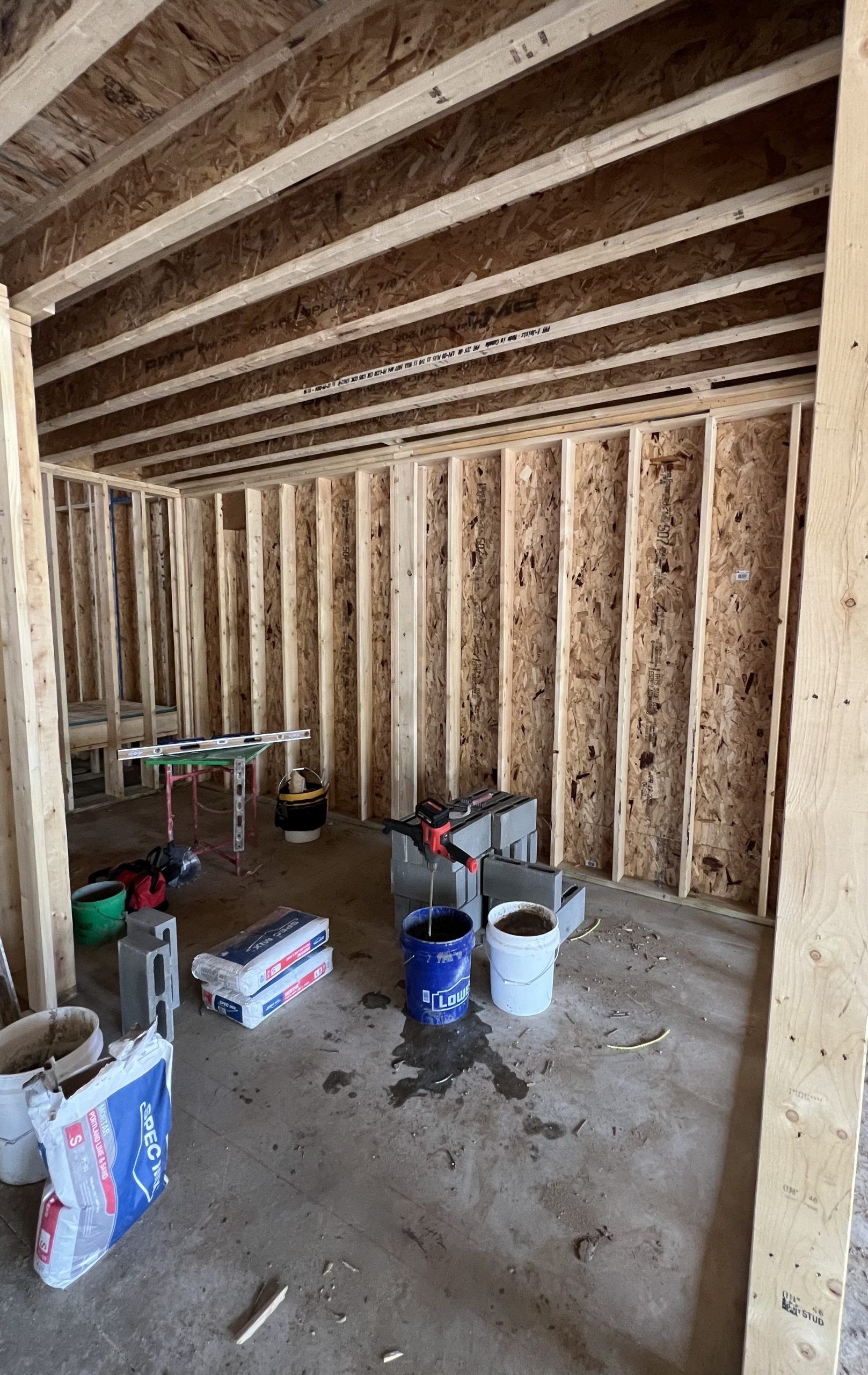 Interior view of a room under construction with exposed wooden studs and beams, and construction materials on the floor.