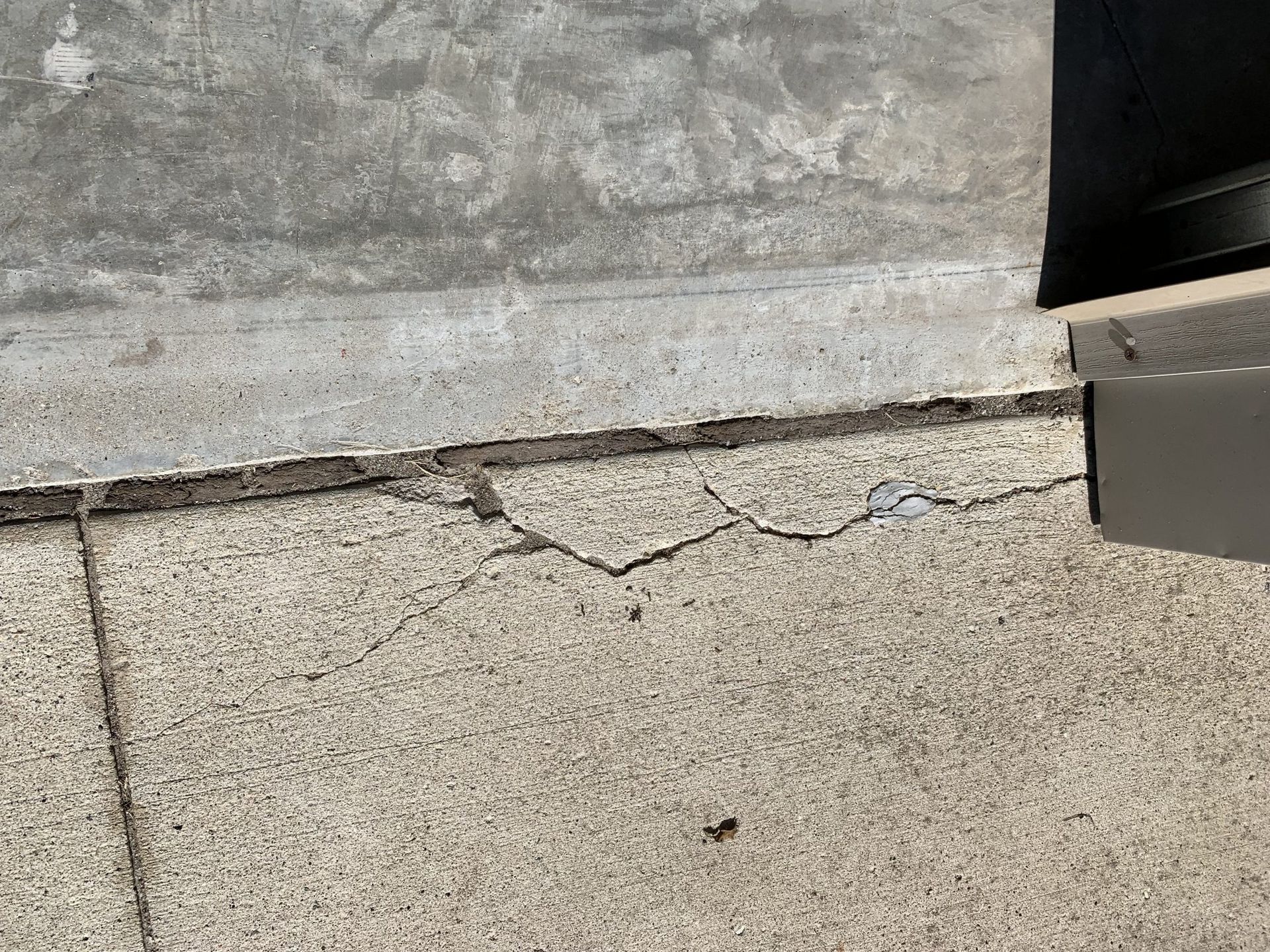 Cracked concrete sidewalk next to a building, possibly due to settling or damage.