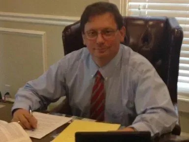 A man in a blue shirt and red tie is sitting at a desk.