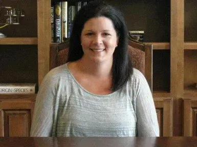 A woman is sitting at a table in front of a bookshelf.