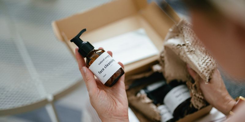 A person is holding a bottle of lotion in front of a box.