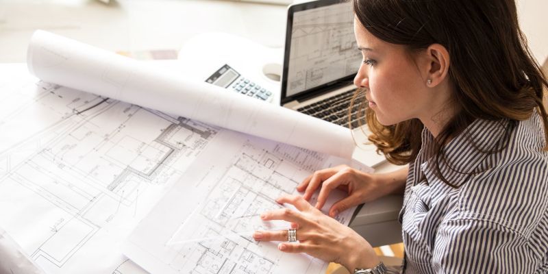 A woman is sitting at a desk looking at a blueprint.