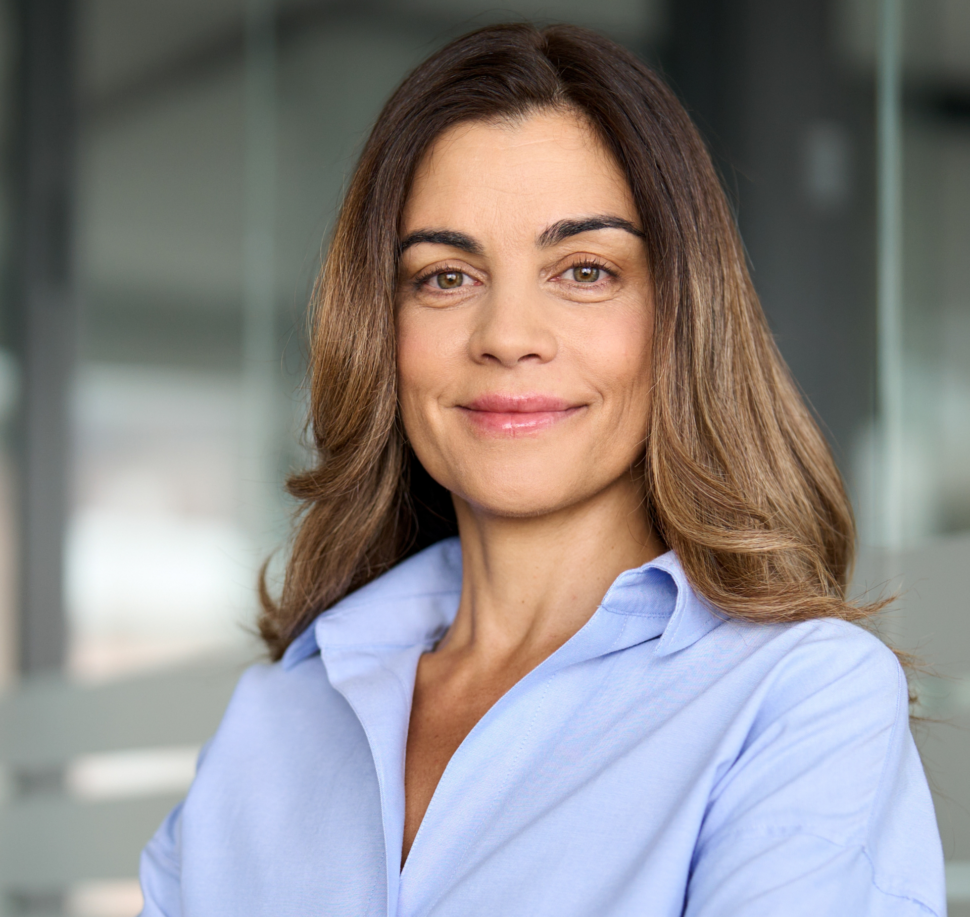 Mujer de cabello castaño con una camisa de cuello azul claro sonriendo en el interior.