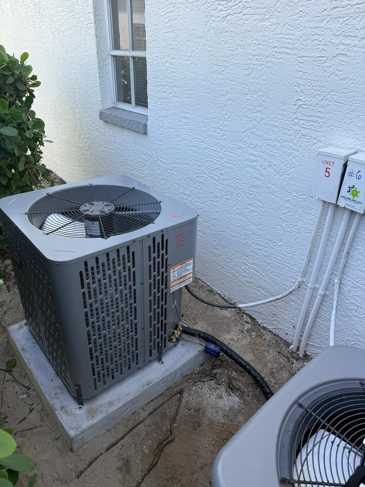 Gray air conditioning unit outside a white building, connected by black tubing.
