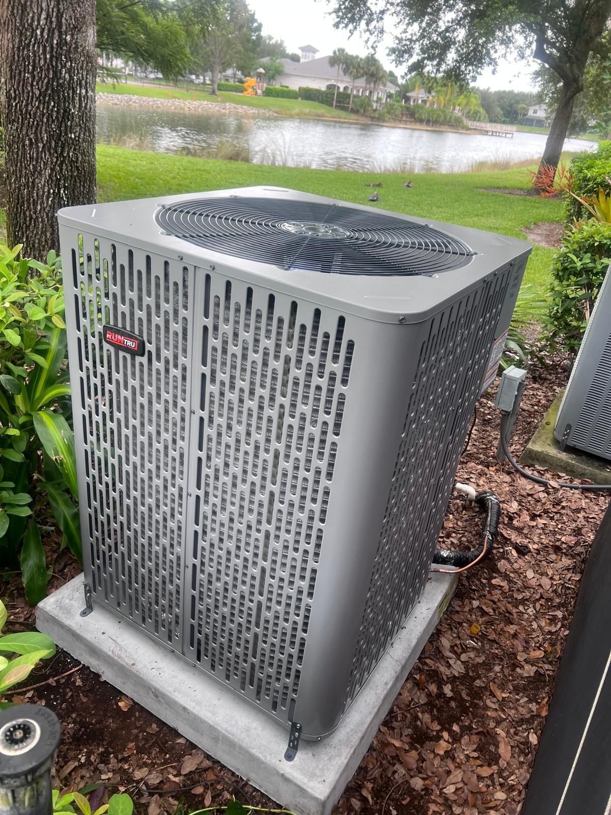 Gray air conditioning unit outside, near a lake.