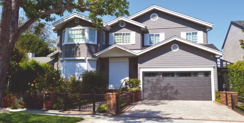 A modern home exterior with a light-colored garage door, a dark front door, stone walls, and a balcony with a black railing.