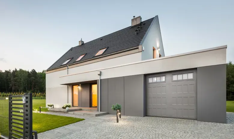 A dark grey, four-panel residential garage door with rectangular window inserts, set against a light stone exterior wall.