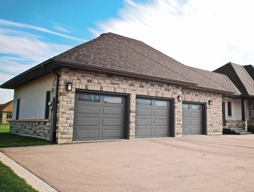 A modern home exterior with a light-colored garage door, a dark front door, stone walls, and a balcony with a black railing.