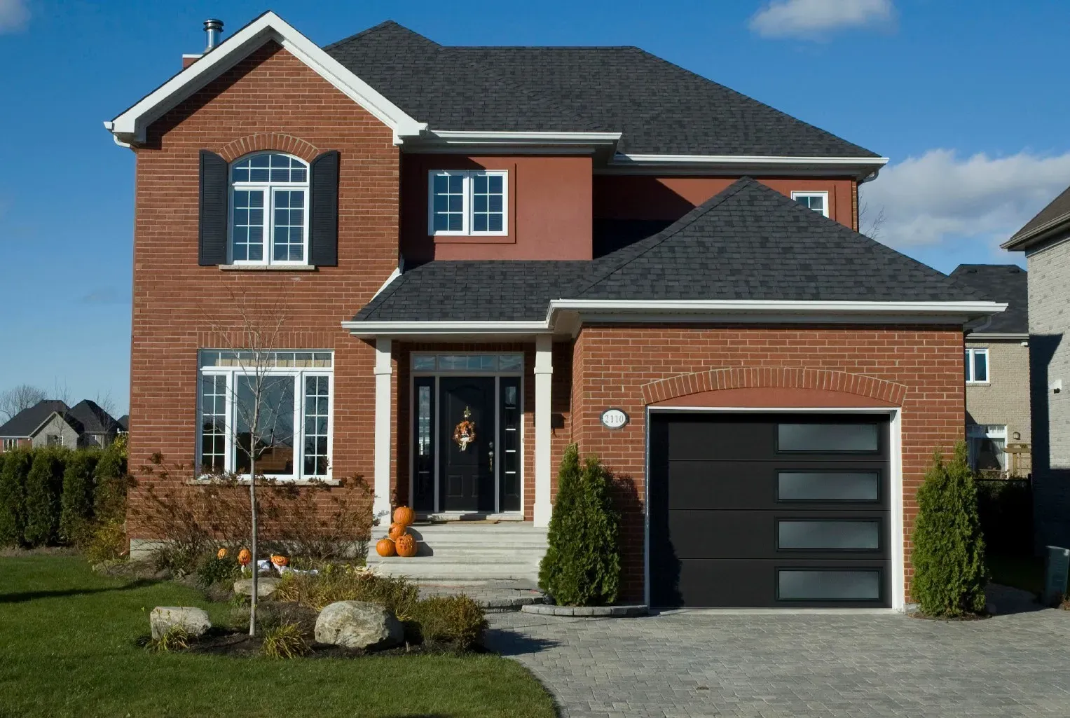A dark grey, four-panel residential garage door with rectangular window inserts, set against a light stone exterior wall.