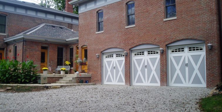 A white garage door with a pergola structure in front of a tan house with a tiled roof.