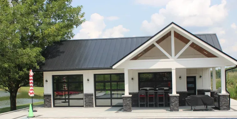 A white garage door with a pergola structure in front of a tan house with a tiled roof.